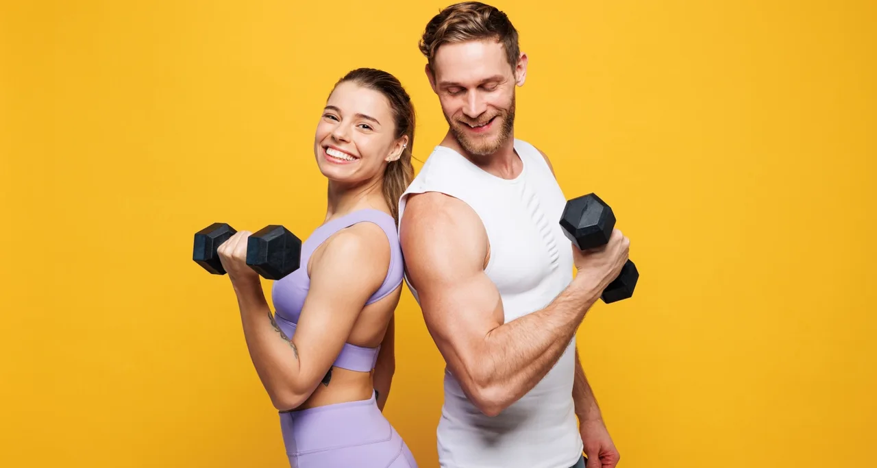 Smiling man and woman standing back-to-back holding dumbbells after a workout